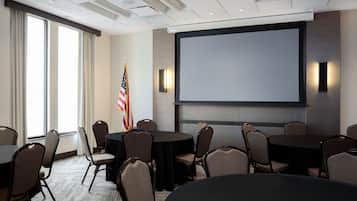 A conference room with a large screen, multiple tables, and chairs.