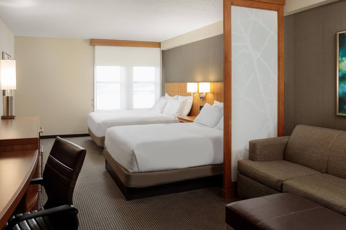 A hotel room with two beds, a desk, a chair, a sofa, and a painting on the wall.