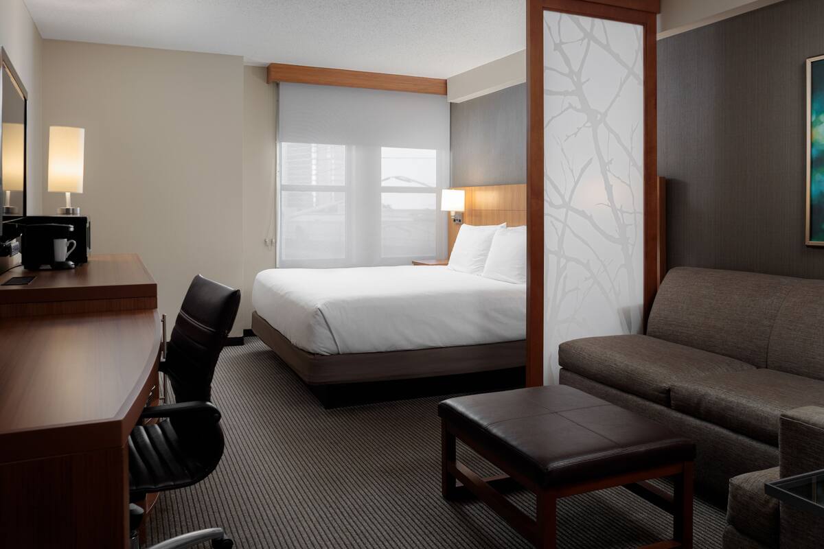 A hotel room with a bed, a desk with a chair, a sofa, and a small table.