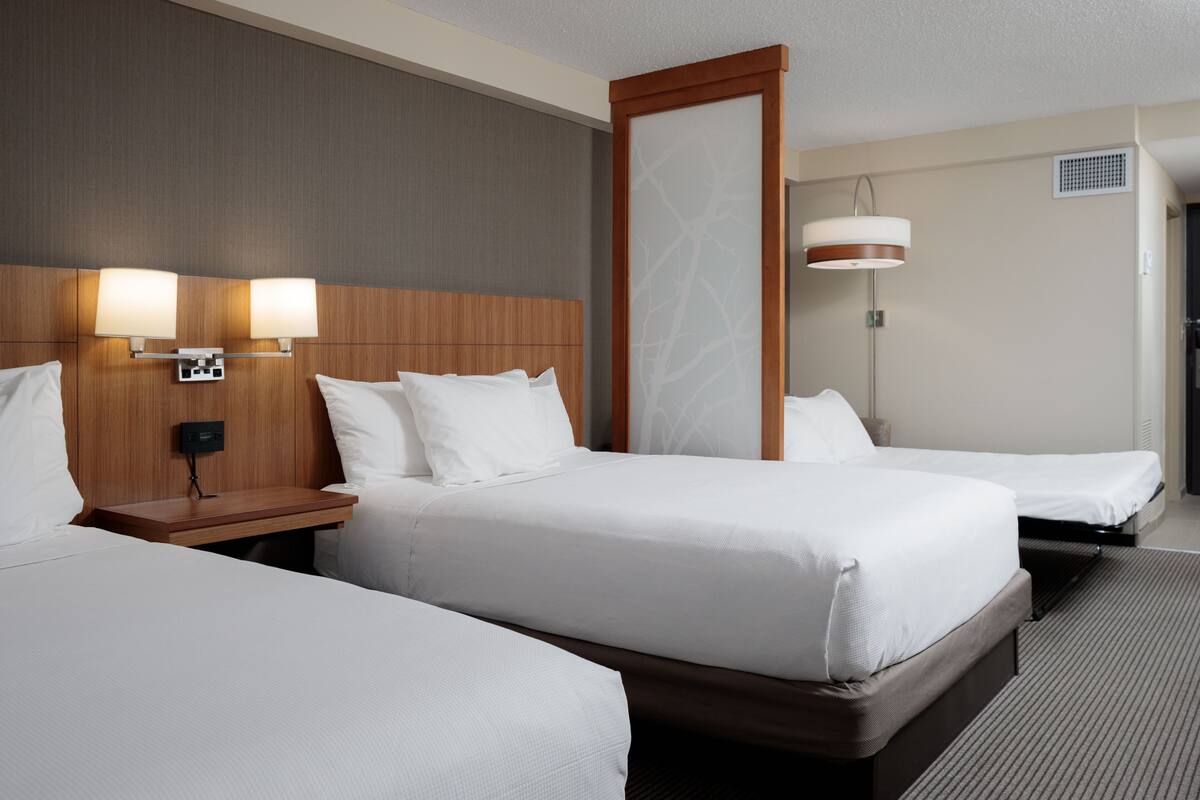 A hotel room with two beds, a wooden headboard, bedside lamps, and a large mirror.