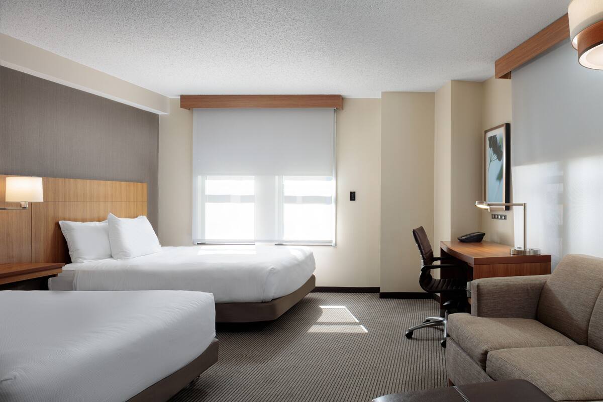 A hotel room with two beds, a desk, a chair, and a sofa.