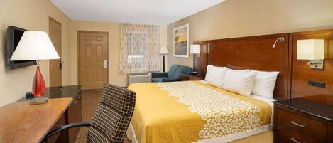 A hotel room with a bed, a desk, a chair, a TV, and a bathroom.