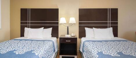 Habitación de hotel con dos camas, cada una con cabecera y mesita de noche con lámpara.