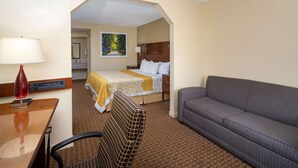 A hotel room with a bed, a sofa, a desk with a lamp, and a chair. - Days Inn by Wyndham Thomaston (Thomaston)