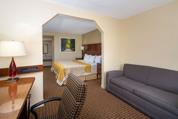 A hotel room with a bed, a sofa, a desk with a lamp, and a chair.