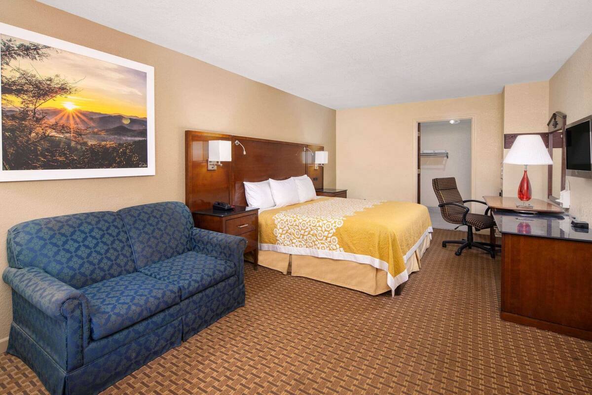 Ein Hotelzimmer mit Bett, Schreibtisch, Stuhl, Sofa und einem Sonnenuntergangsgemälde.