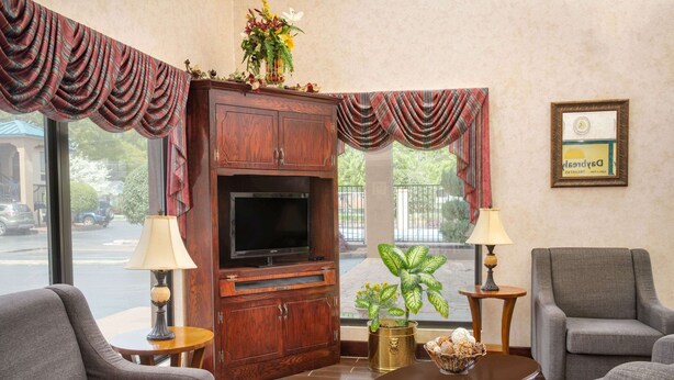 A hotel lobby with a wooden cabinet, television, two armchairs, a round coffee table, and a potted plant. - Days Inn by Wyndham Thomaston (Thomaston)