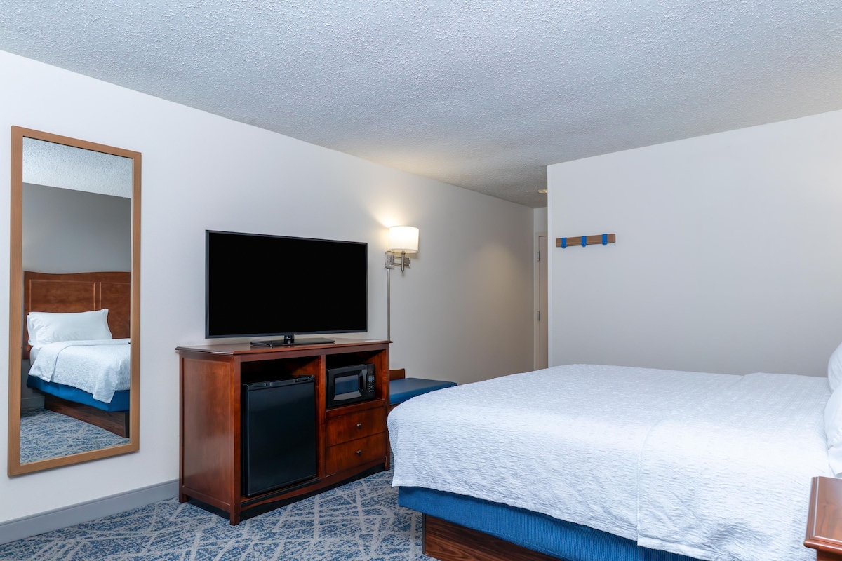 A hotel room with a bed, a television, a mirror, a microwave, and a small cabinet.