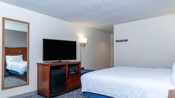 A hotel room with a bed, a television, a mirror, a microwave, and a small cabinet.