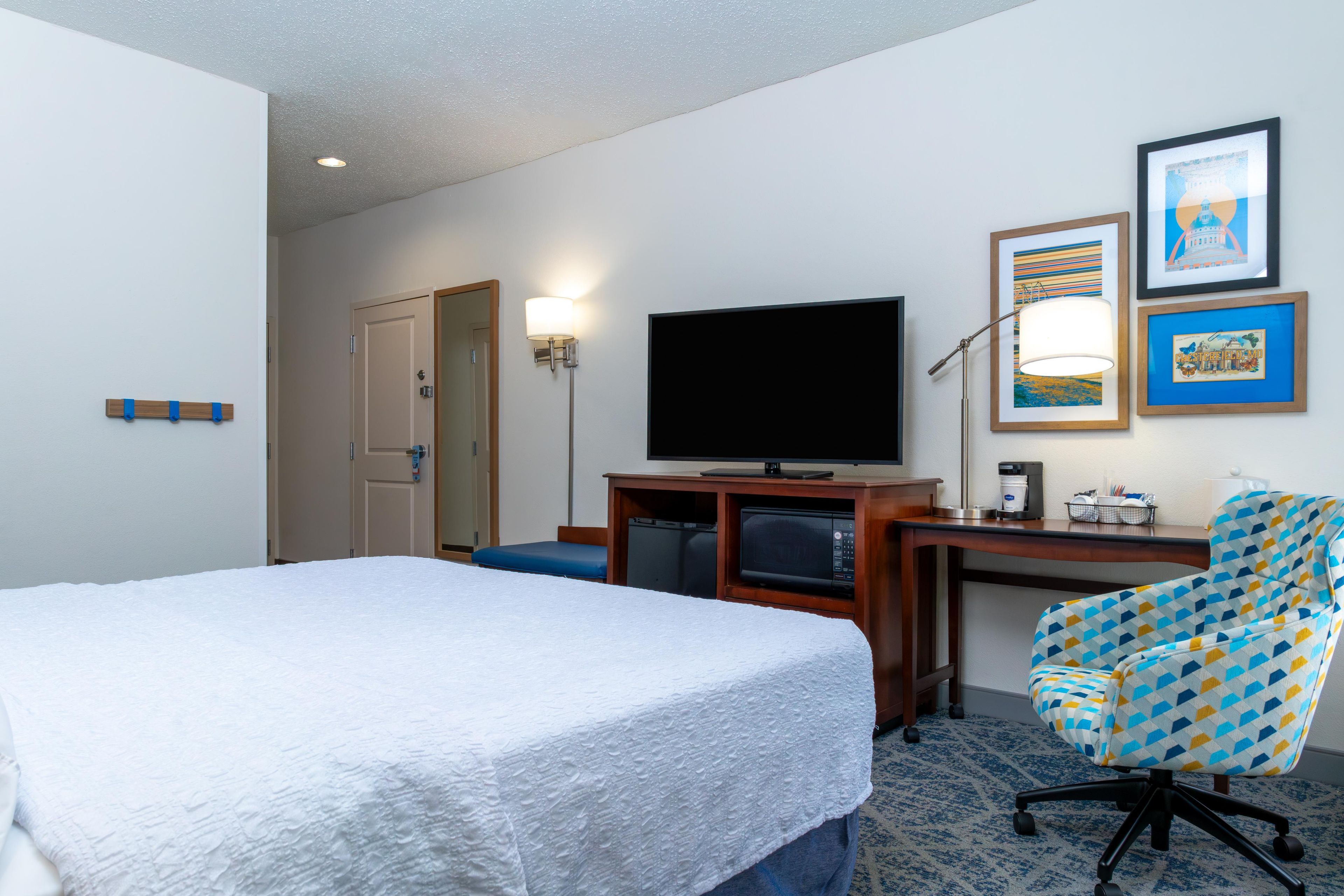 A hotel room with a bed, a desk with a television, a chair, and a coffee machine.