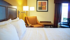 A hotel room with a large bed, a desk, a chair, and a lamp.