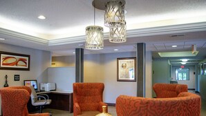 A lobby with patterned orange chairs, a round table with a decorative vase, and two hanging lamps.