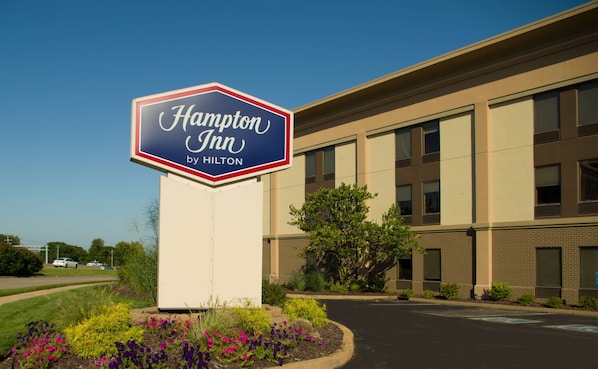 A Hampton Inn by Hilton sign in front of a building with a brick facade and multiple windows.