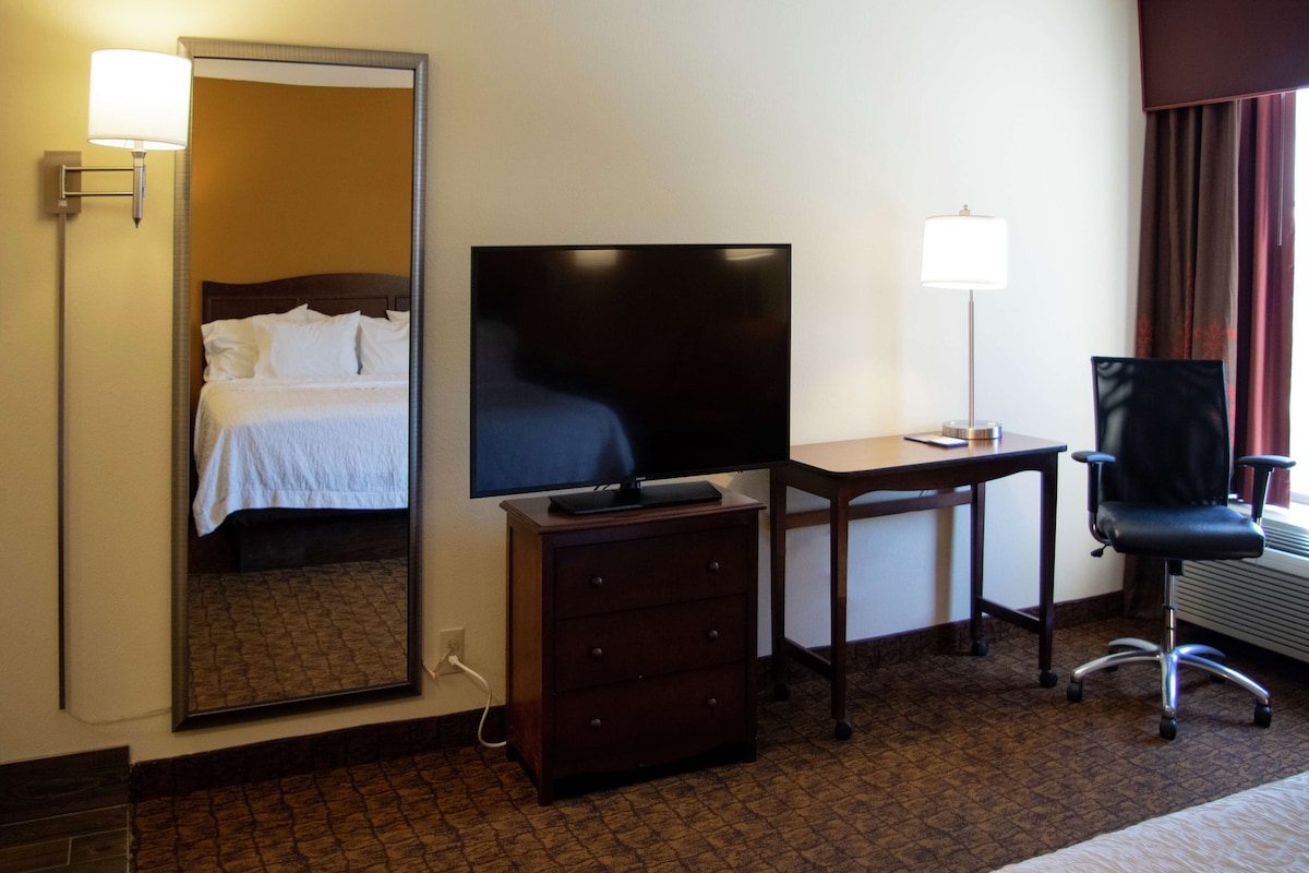 A hotel room with a bed, a television, a desk with a lamp, a chair, and a dresser.