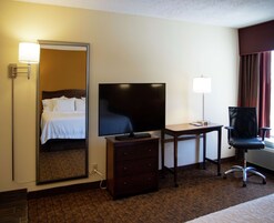 A hotel room with a bed, a television, a desk with a lamp, a chair, and a dresser.