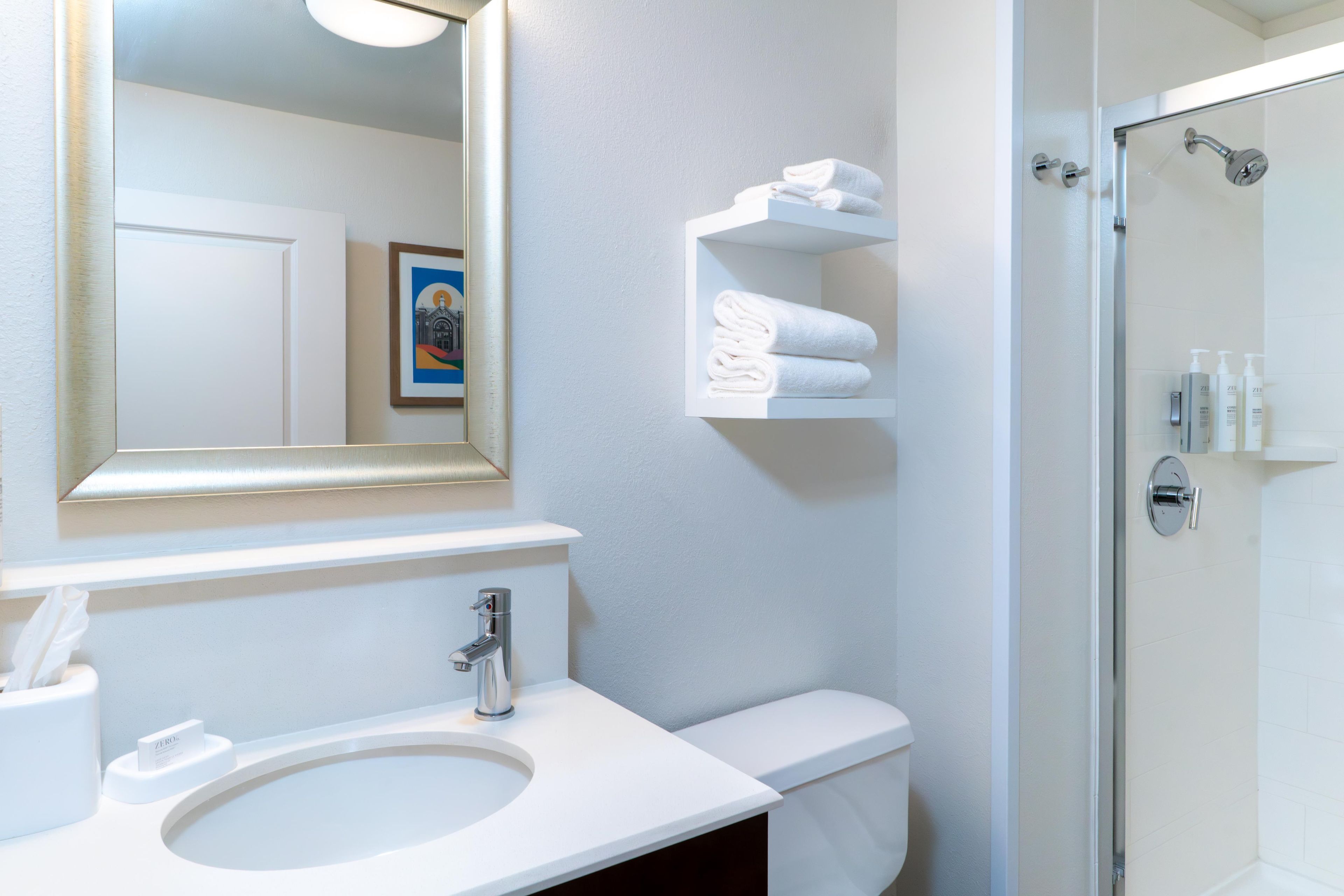 A bathroom with a sink, mirror, toilet, and a shower area.