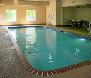 An indoor swimming pool with clear water, a lifeguard chair, and a poolside area with chairs and a table.