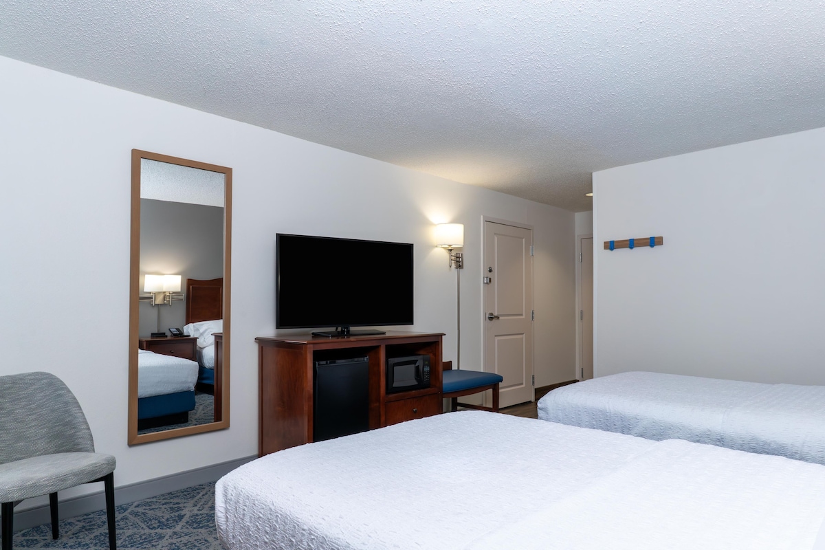 A hotel room with two beds, a television, a desk with a computer, a chair, and a mirror.