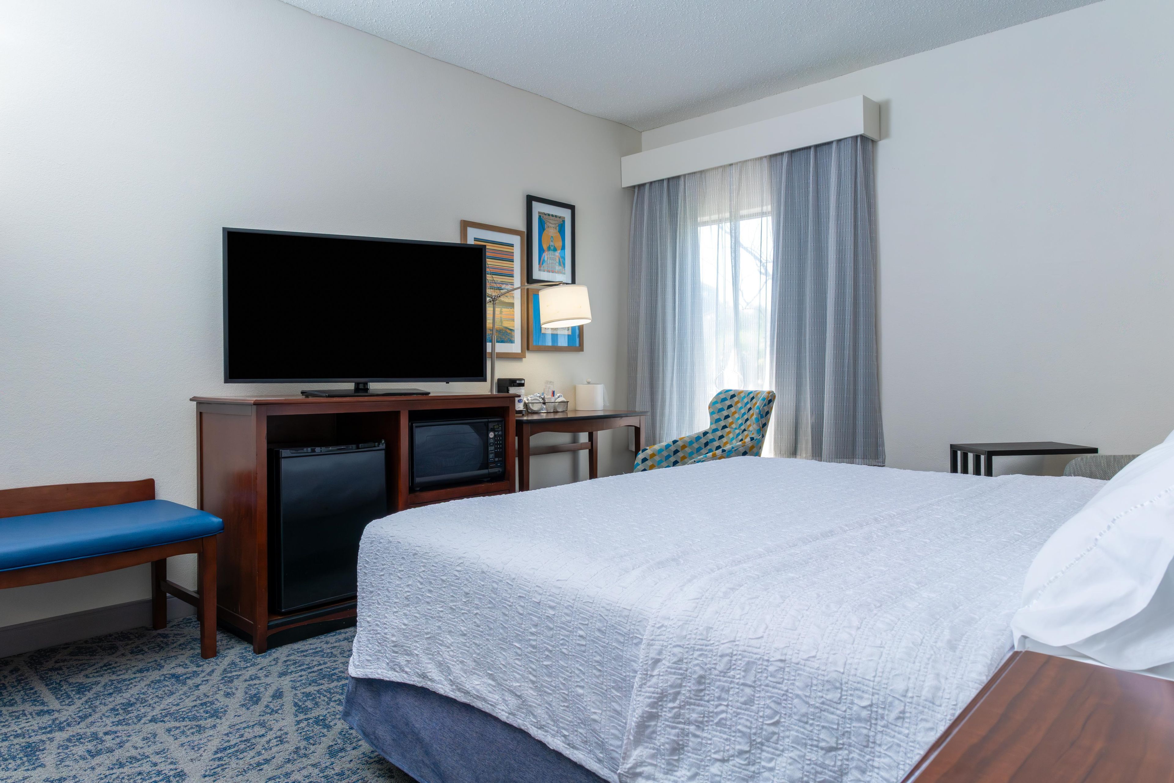 A hotel room with a bed, a television, a desk, a chair, and a microwave.