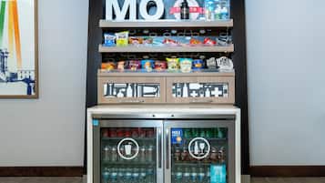 Máquina expendedora con aperitivos y bebidas, incluyendo Coca-Cola y Sprite, y un refrigerador debajo.