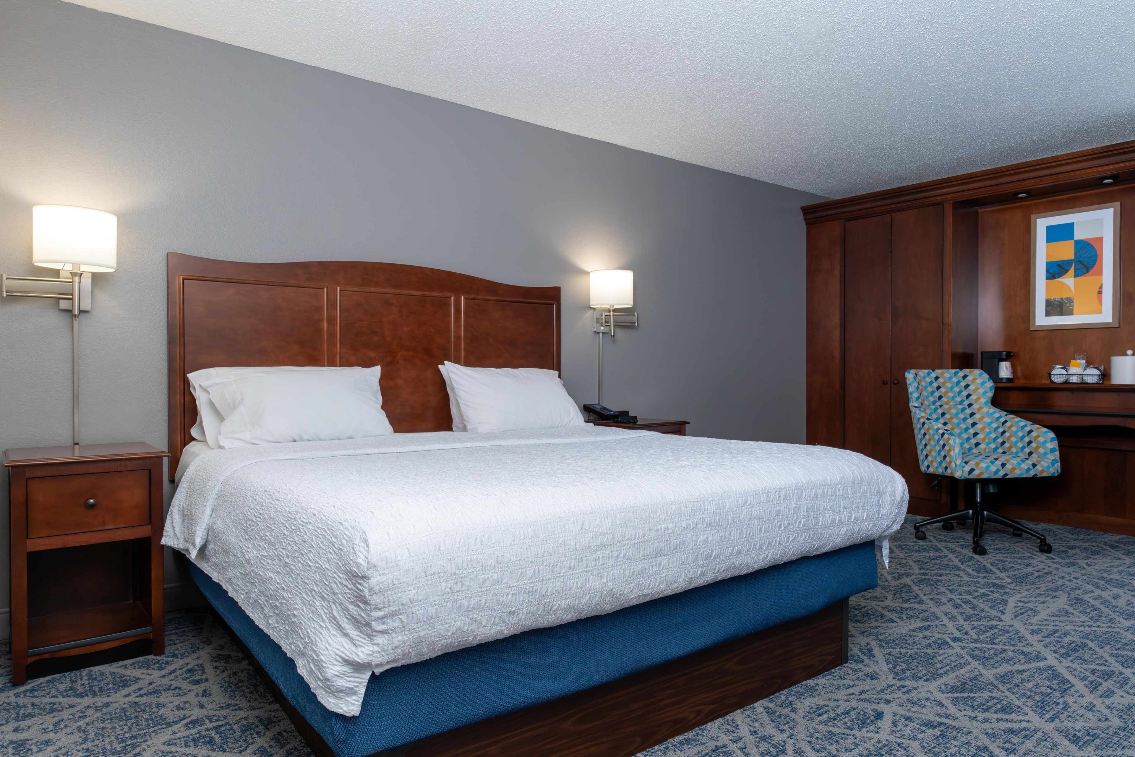 Une chambre d’hôtel avec un grand lit, deux tables de chevet, un bureau avec une chaise et une lampe fixée au mur.