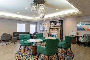 A modern lounge area with green upholstered chairs, a coffee table, a vending machine, and a wall-mounted refrigerator. - Hampton Inn St. Louis/Chesterfield (Chesterfield)