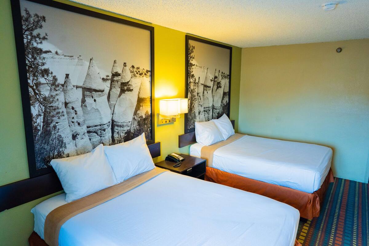 Ein Hotelzimmer mit zwei Betten, einem Nachttisch mit Lampe und einem großen gerahmten Bild an der Wand.