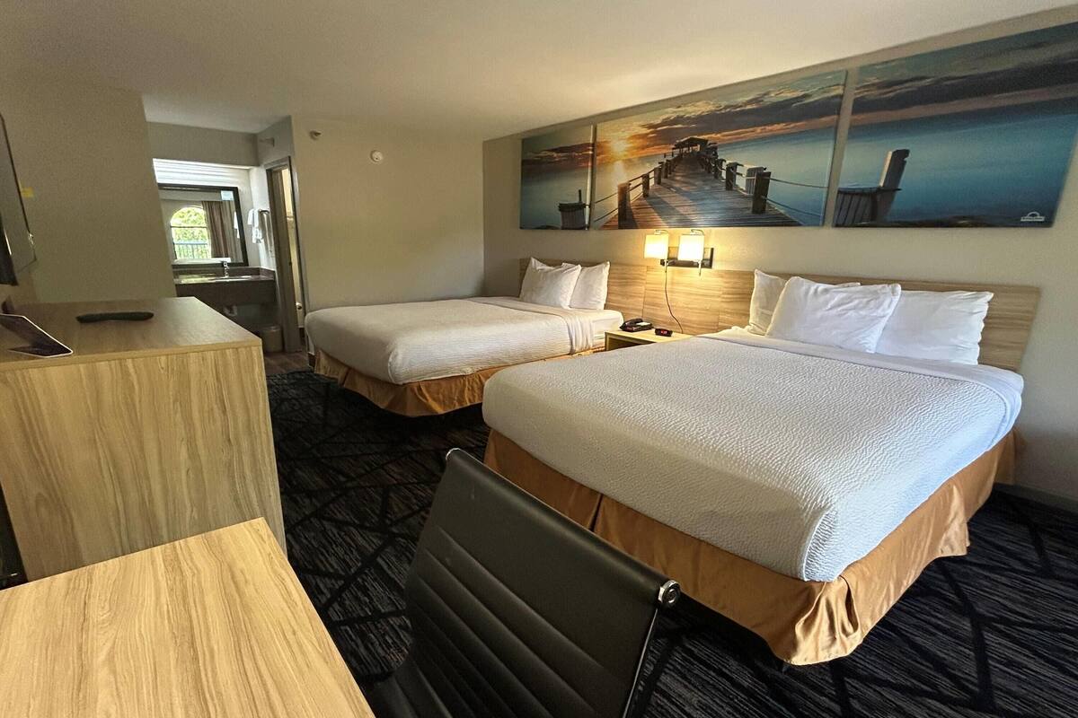 Ein Hotelzimmer mit zwei Betten, einem Schreibtisch, einem Stuhl und einem Gemälde eines Piers.