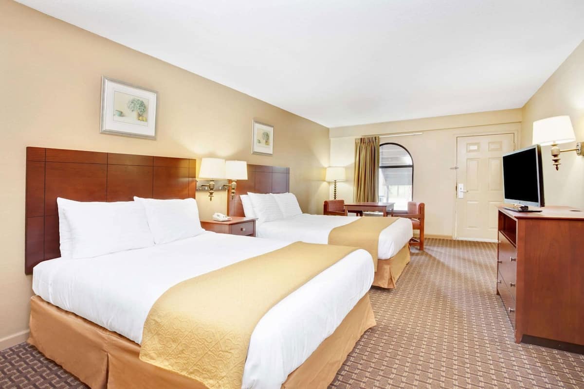 Ein Hotelzimmer mit zwei Betten, einem Schreibtisch, einem Fernseher und einer Tür.