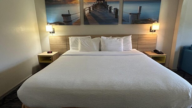 A hotel room with a large bed, two bedside tables, and a wall-mounted painting of a pier. - Days Inn & Suites by Wyndham Stockbridge South Atlanta (Stockbridge)