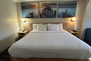 A hotel room with a large bed, two bedside tables, and a wall-mounted painting of a pier. - Days Inn & Suites by Wyndham Stockbridge South Atlanta (Stockbridge)