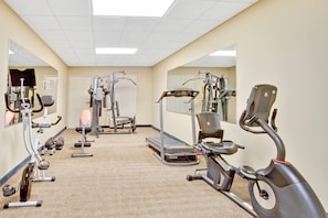 Een fitnessruimte met cardiotoestellen, krachttrainingsapparatuur en losse gewichten.