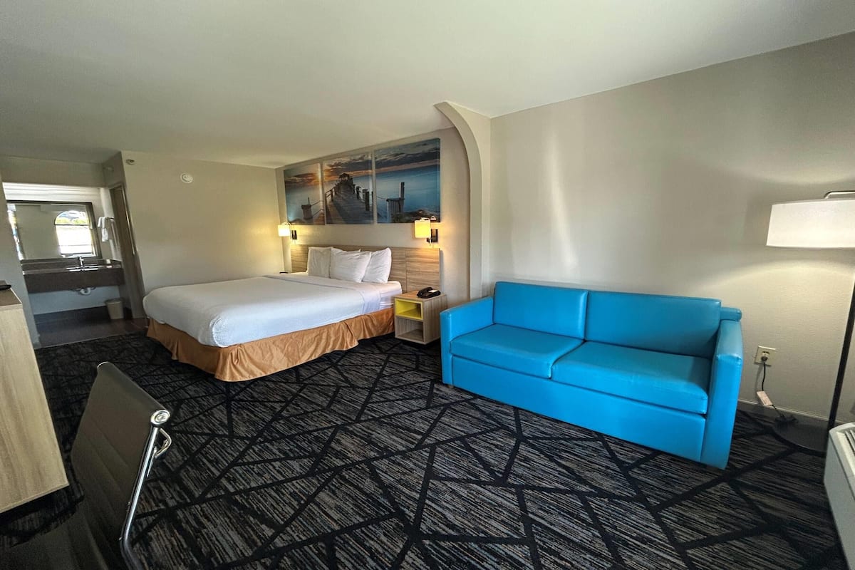 Ein Hotelzimmer mit einem Bett, einem blauen Sofa, einem Schreibtisch und einem Bild an der Wand.