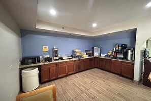 A kitchen with wooden cabinets, a microwave, coffee maker, and a refrigerator. - Days Inn & Suites by Wyndham Stockbridge South Atlanta (Stockbridge)