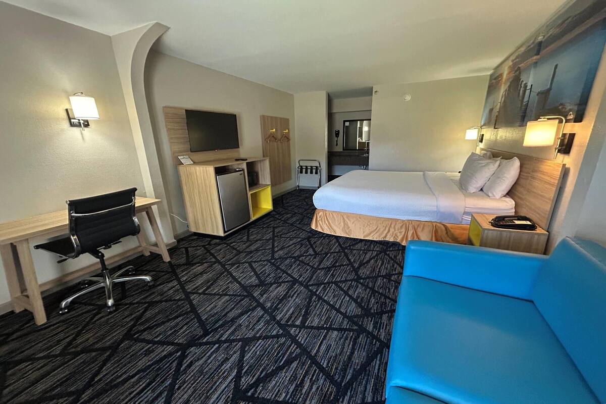 Ein Hotelzimmer mit Bett, Schreibtisch mit Stuhl, Fernseher und einem durchgegangenen Tür sichtbaren Badezimmer.
