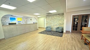 A reception area with a stone wall, a reception desk, two armchairs, and a wooden floor. - Days Inn & Suites by Wyndham Stockbridge South Atlanta (Stockbridge)
