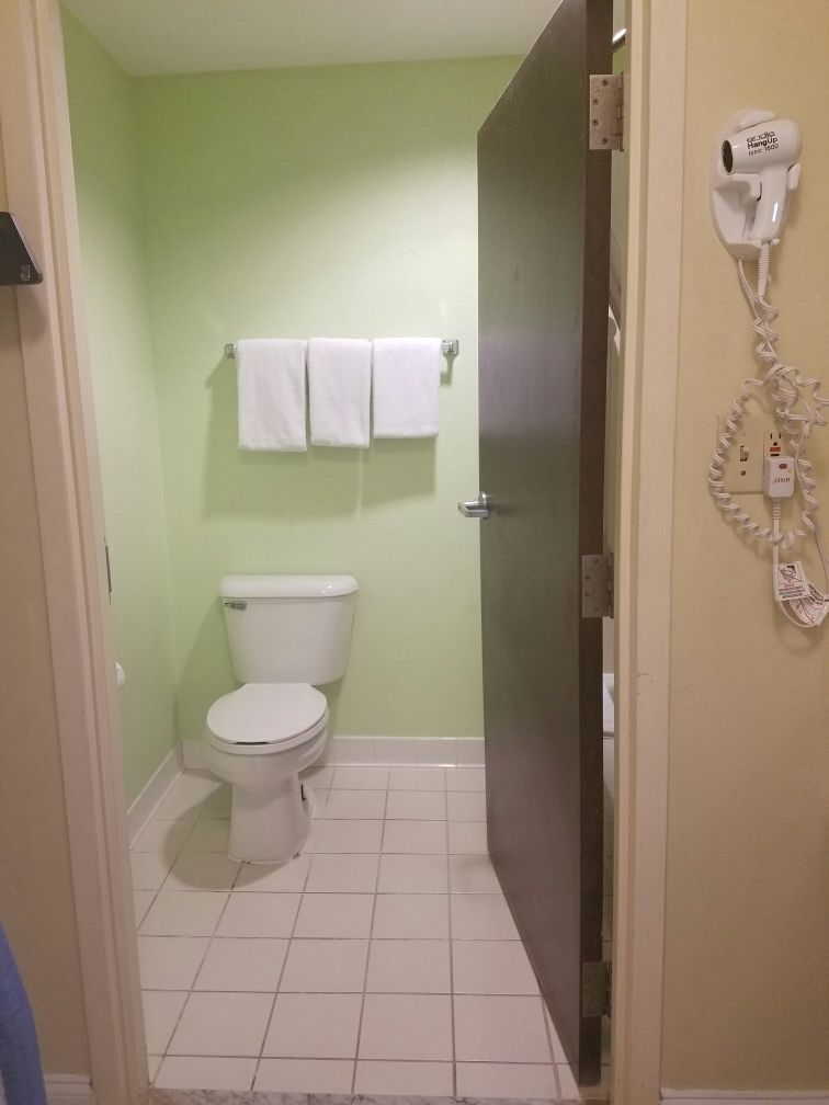 A bathroom with a toilet, a towel rack with two white towels, and a hairdryer mounted on the wall.