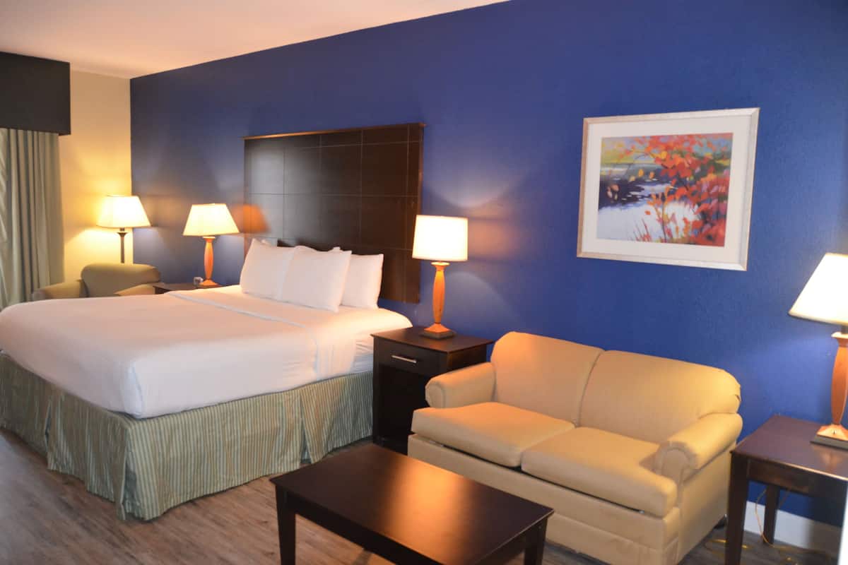 A hotel room with a large bed, two bedside tables with lamps, a sofa, a coffee table, and a painting on the wall.