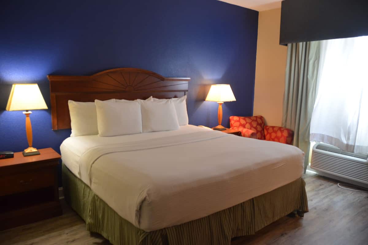 A hotel room with a large bed, two bedside lamps, a red chair, and an air conditioning unit.