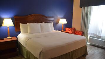 Quarto de hotel com uma cama grande, duas luminárias de cabeceira, uma cadeira vermelha e um ar condicionado.