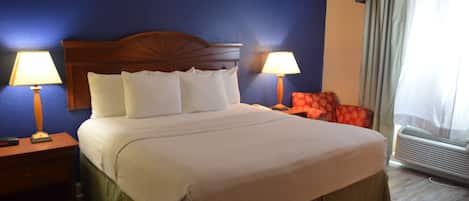 A hotel room with a large bed, two bedside lamps, a red chair, and an air conditioning unit.