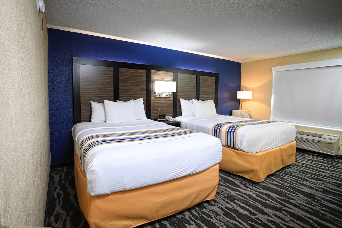A hotel room with two beds, a large headboard, a flat-screen TV, and a wall-mounted heater.