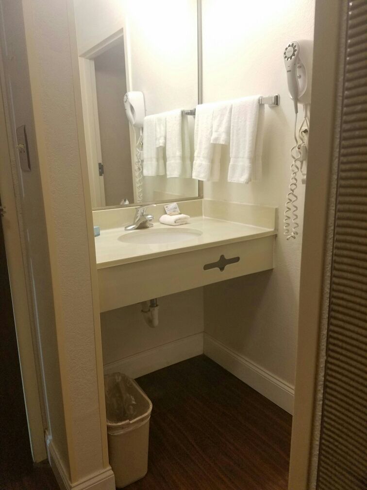 Une salle de bain avec un lavabo blanc, un miroir, un porte-serviettes, un sèche-cheveux et une poubelle.