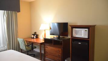 Quarto de hotel com cama, escrivaninha com computador, televisão, micro-ondas e frigorífico.
