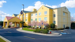 A yellow multi-story hotel with a red-roofed entrance, a parking lot, and blooming trees. - Eagles Nest Inn (Statesboro)
