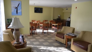 A hotel room with a dining area, a TV mounted on the wall, and a lamp on a side table. - Eagles Nest Inn (Statesboro)