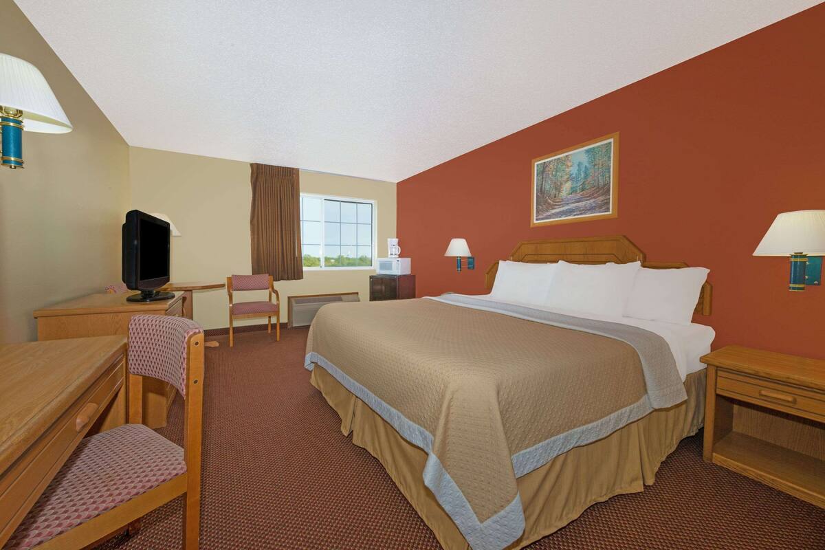Ein Hotelzimmer mit Bett, Schreibtisch, Stuhl, Fernseher und Fenster.