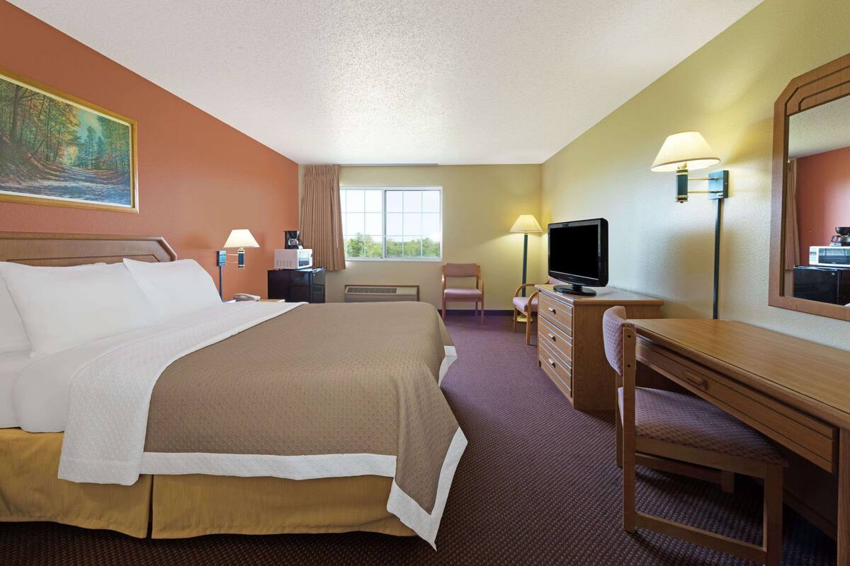 Ein Hotelzimmer mit einem großen Bett, einem Schreibtisch, einem Fernseher und einem Fenster mit Vorhängen.