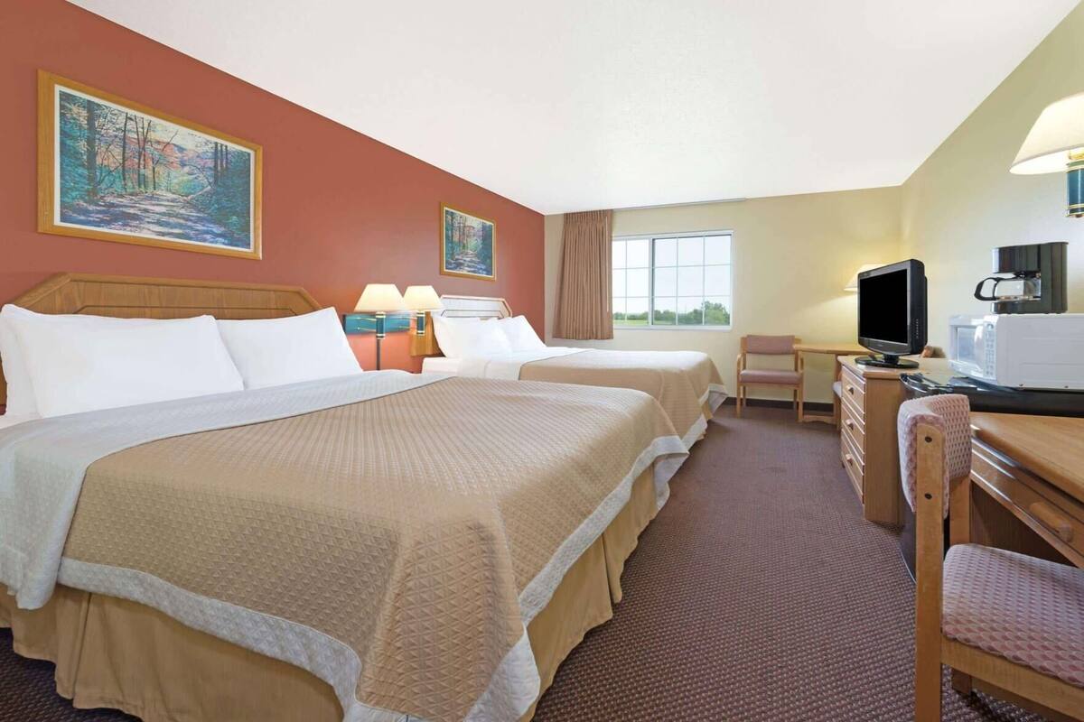 Ein Hotelzimmer mit zwei Betten, einem Schreibtisch mit Fernseher, einem Sessel, einem Fenster und Bildern an den Wänden.