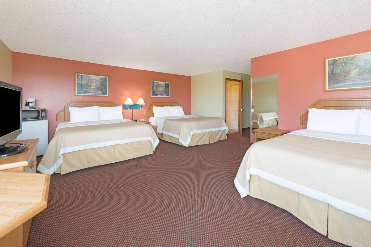 Ein Hotelzimmer mit drei Betten, einem Fernseher, einem Schreibtisch und einer Mikrowelle.